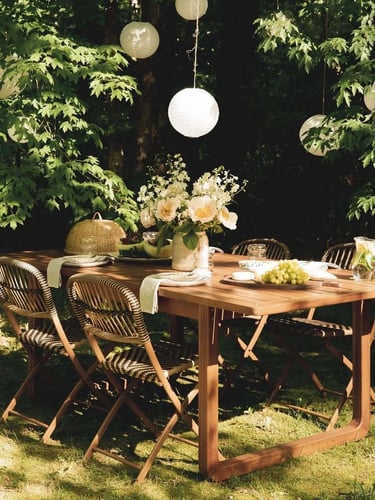 Garden seating area with wooden outdoor table, natural shade, green plants and relaxed dining setup