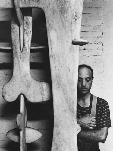 Black and white photograph of an artist beside a large abstract sculpture, showing the connection be