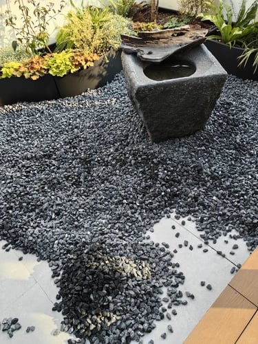 Small garden corner with gravel flooring, stone water basin, wood details, and simple outdoor materi