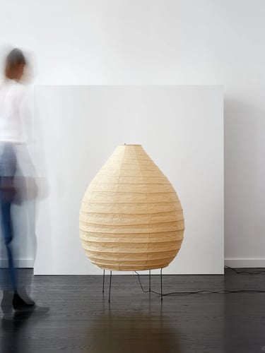 Single Akari paper lamp glowing softly beside a blurred figure, showing the quiet atmosphere of Nogu