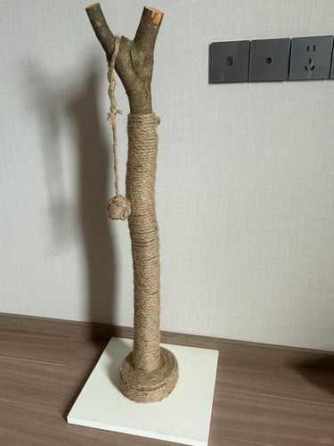 Tall natural wood and sisal cat scratching post with a hanging ball toy, designed for climbing and s