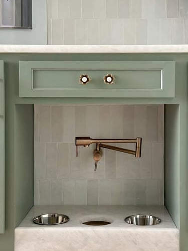 Built-in pet feeding station with stainless steel bowls, a small faucet and soft green cabinetry for