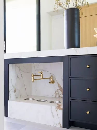 Elegant built-in cat feeding station with food bowls, marble-style wall, brass faucet and dark stora