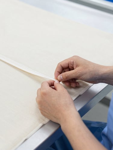 Close-up, slightly angled shot of a skilled textile worker's hands meticulously inspecting the stitching of a medical scrub on a bright, clean factory floor. Crisp commercial photography, bright clinical studio light, sharp focus.