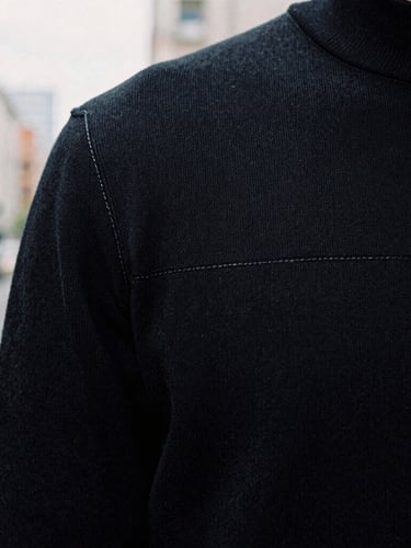 Extreme close-up of double-stitched seams on a heavy black knit fabric, soft overcast daylight, highlighting the clean structural texture, 35mm film.
