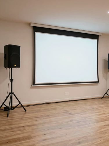 Wide shot of an indoor event space mid-setup from left side, professional sound speakers on tripod stands and a large projection screen erected at the far end, cables neatly run across the floor, bright neutral studio lighting, no people, documentary straight-on framing