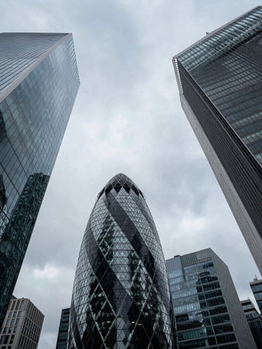 Dramatic low-angle architectural perspective of London financial district skyscrapers under diffused overcast daylight, sharp structural lines cutting into a soft sky.