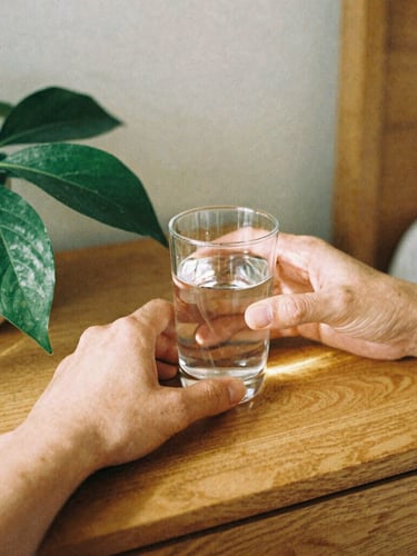 Detail of hands placing a glass of water next to a green plant on a wooden bedside table, warm morning light, soft shadows, 35mm film look.