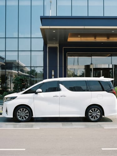 Side profile of a pristine white Toyota Alphard parked in front of a modern glass executive terminal in Batam, bright natural daylight, clean reflections, elegant navy tones, professional 35mm photography.