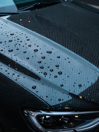 Extreme macro close-up of water droplets bead-sliding off a highly reflective, carbon-fiber car hood protected by BASF Rodim film, cool cyan highlights