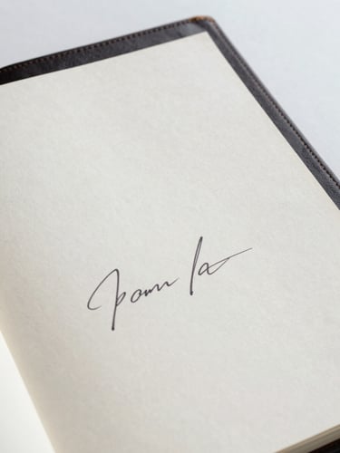Close-up of a hand-signed certificate of provenance on heavy cotton paper, resting next to a leather-bound artist monograph, soft studio daylight