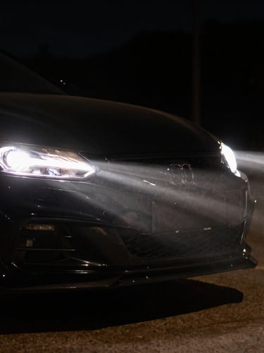 Dramatic automotive photography of car headlights piercing through deep night shadows, warm headlight glow, high-contrast street lighting, sharp focus, 35mm lens