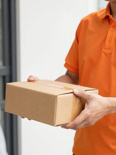 Close-up of a delivery rider in a bright orange shirt handing over a brown package to a customer at a doorstep, bright daylight, sharp focus
