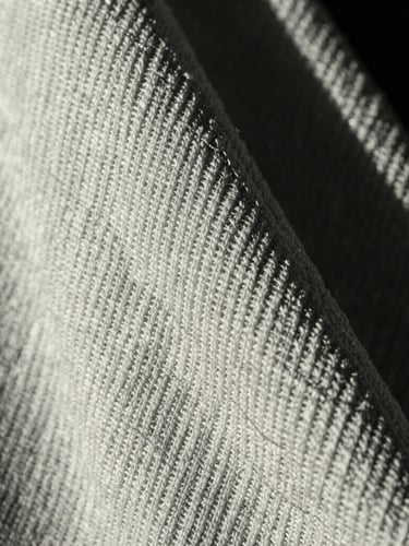 Macro close-up of heavy 400GSM loopback terry fabric texture, showing the dense knit structure and clean engineered stitching, high-contrast dramatic side-lighting, monochrome tones.