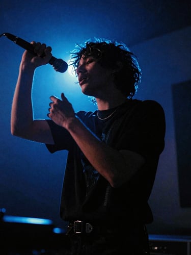 Dynamic low-angle portrait of a musical artist performing in a moody, low-key studio environment with electric blue backlighting, 35mm film grain style.