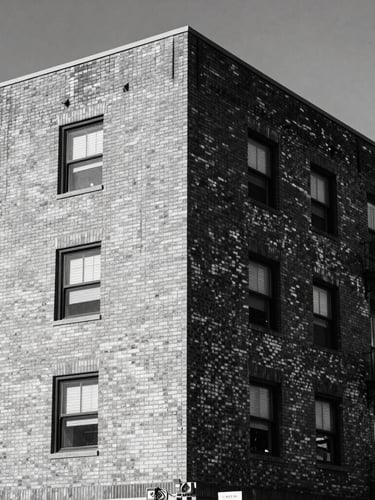 Gritty editorial portrait of a brick residential building under harsh midday Texas sunlight, high-contrast desaturated tones, sharp architectural details, 35mm lens.