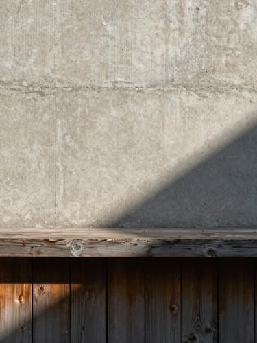 Straight-on architectural detail of raw concrete and weathered pine wood, soft afternoon shadow casting a sharp diagonal, minimalist composition.