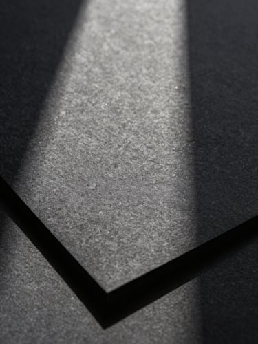 Extreme close-up of tactile printed stationery on heavy textured charcoal paper stock, casting long dramatic shadows under harsh natural light