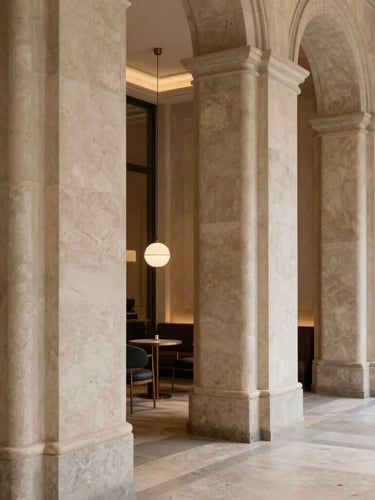 Warm architectural photography of a boutique hotel lobby in Milan, elegant travertine stone columns, soft ambient lighting, 35mm