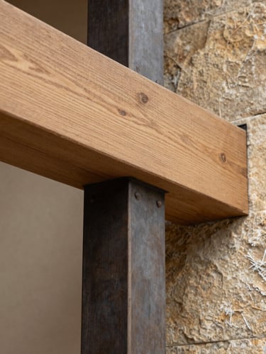 Macro architectural photograph of a sharp material transition where a sandblasted oak beam meets a raw steel column, natural side-lighting, warm stone tones, sharp focus.