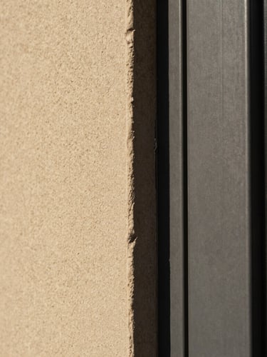 Macro shot of a hand-applied lime plaster finish meeting a dark steel door frame, warm stone and charcoal tones, sharp focus.