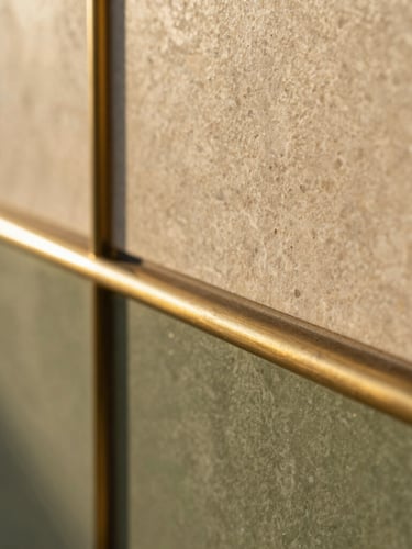 Tactile macro shot of premium architectural finishes, natural stone and brushed brass detailing, warm morning light, shallow depth of field.