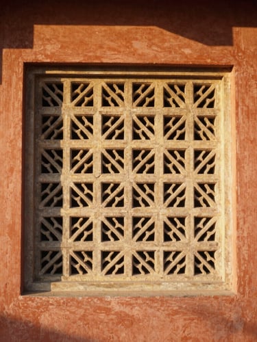 A sun-drenched architectural crop of a stone-carved jali screen at Hotel Grand Capitol, warm golden hour light casting soft shadows on terracotta walls, 35mm photography