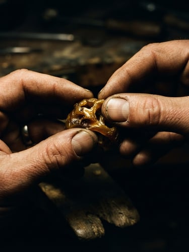 Extreme close-up, high-contrast editorial photography, dramatic side-lighting, deep shadows, rich gold tones, tactile skin texture, 35mm, designer's hands shaping heavy molten wax models, detailed texture of wax and hands.