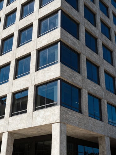 Wide architectural angle of a modern concrete corporate building facade in Fort Myers, hard bright direct sunlight, sharp geometric shadows, electric blue glass reflections, 35mm.