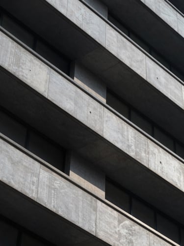 A close-up of a high-contrast architectural facade with sharp geometric shadows and clean lines, emphasizing structure and scale under cool diffused light.