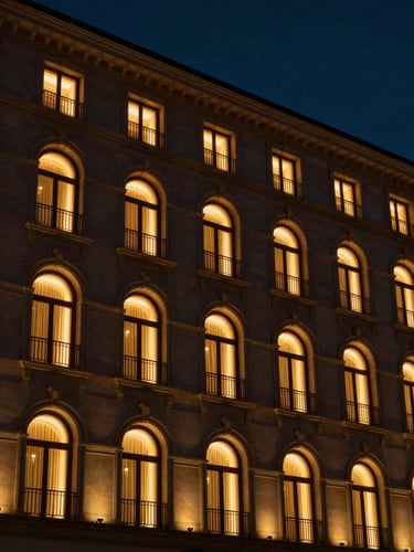 Dramatic architectural detail of a luxury boutique hotel facade at golden hour, warm ambient light glowing from arched windows against a deep navy twilight sky.