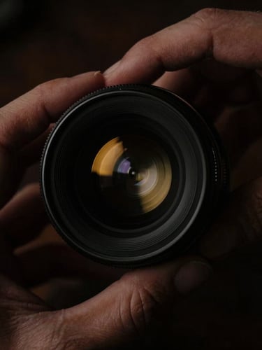 cinematic film photography, low-key dramatic chiaroscuro lighting, deep shadows, rich dark tones, anamorphic lens, 35mm. Extreme macro close-up of hands adjusting a vintage cinema lens, gold highlight reflections, rich textures