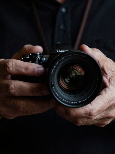 Moody close-up of a director's hands adjusting a vintage anamorphic lens, dramatic side lighting, deep shadows, rich dark tones, 35mm film look.
