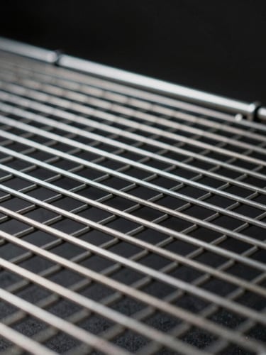 Close-up of industrial steel mesh grid, high-contrast side lighting highlighting the metallic sheen and clean geometric lines, dark studio background.