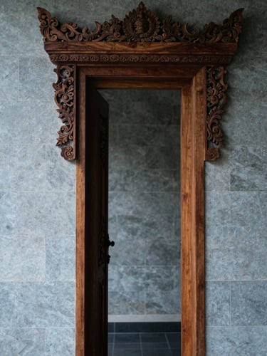 Interior architectural detail of a Balinese villa—carved wooden door frame in sharp focus, cool north-facing daylight, textured stone wall behind, no people, minimal and composed