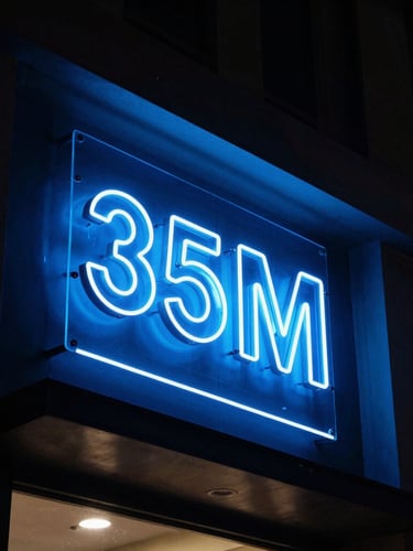Dramatic night-time architectural photography of a glowing 3D acrylic sign board on a modern shop facade in Hyderabad, intense electric blue neon illumination, high-contrast dark-mode aesthetic, 35mm lens