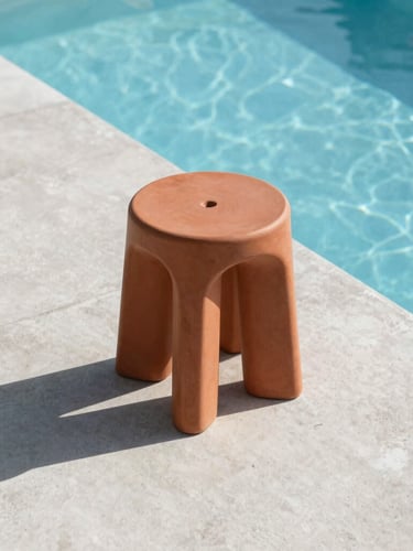 Low-angle architectural shot of a monolithic terracotta resin stool cast in sharp midday sunlight by a clean concrete pool edge, graphic shadows, 35mm
