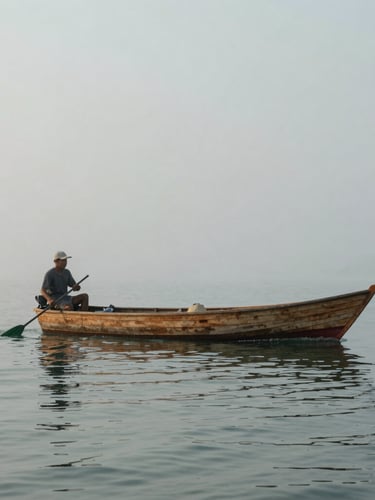An environmental portrait of a waterman steering a wooden deadrise boat through calm morning mist, soft gray and green tones.