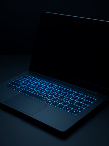 Sleek matte black laptop on a dark desk with sharp neon blue lighting reflecting on the keyboard, minimalist tech photography