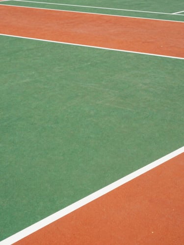 Tight top-down architectural grid of a freshly painted pickleball court, showing crisp white boundary lines on bright green and orange surfaces.