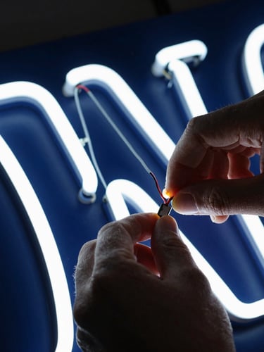 Macro shot of the fabrication process of an illuminated sign, hands adjusting LED wiring inside a corporeal letter, dramatic contrast, navy tones, 50mm lens