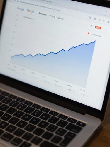 Overhead close-up of a laptop screen displaying a Google Analytics dashboard with a sharply rising organic traffic curve, cool studio lighting, keyboard partially visible at bottom frame, no people