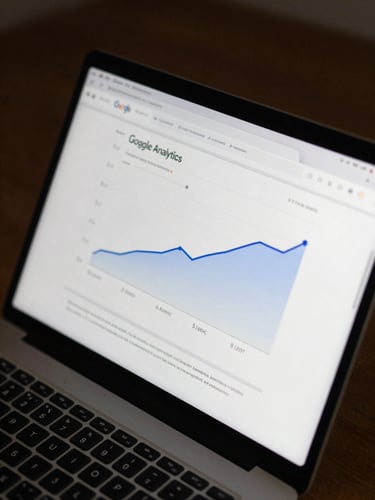 Tight overhead close-up of a laptop screen displaying a Google Analytics dashboard with upward-trending organic traffic curves, cool even studio lighting, dark desk surface visible at edges, no people