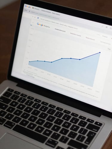 Overhead tight close-up of a laptop screen displaying a Google Analytics dashboard with organic traffic growth curve trending sharply upward, cool studio lighting, dark desk surface visible at edges, no people