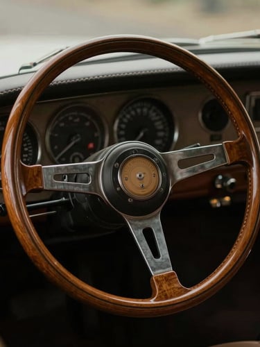 Close-up detail of a classic wooden steering wheel and hand-stitched leather dashboard of a rare vintage automobile, warm low-key natural light