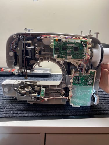 A sewing machine with the outside covers removed, revealing the inside of a computerized machine. 