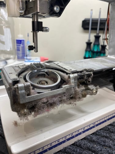 The bobbin area of a sewing machine with covers removed, revealing a large build-up of dust and lint