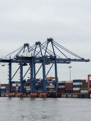 Wide shot of a modern deep-water container terminal with massive blue gantry cranes under a cool overcast sky, desaturated navy and grey tones, crisp industrial photography