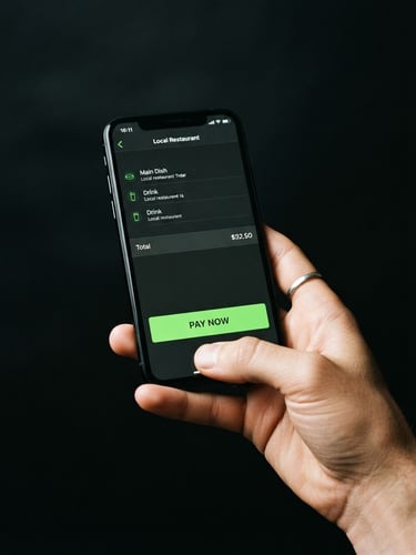 Crisp studio shot of a hand holding an iPhone showing a local restaurant checkout screen with clear green pay buttons, dark obsidian background, 35mm photography