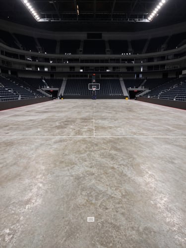 Wide environmental shot looking down the length of a large sports arena floor after cleaning, neutral overhead lighting, empty seating tiers receding into background, polished concrete visible in foreground